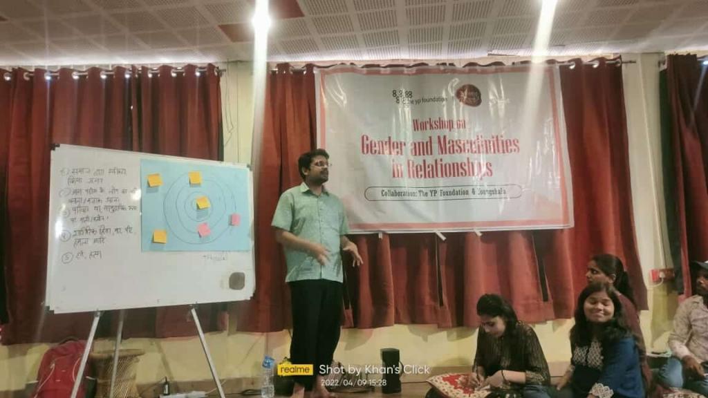 facilitator conducting a training session with a banner behind them reading "Gender and Masculinities in Relationships"