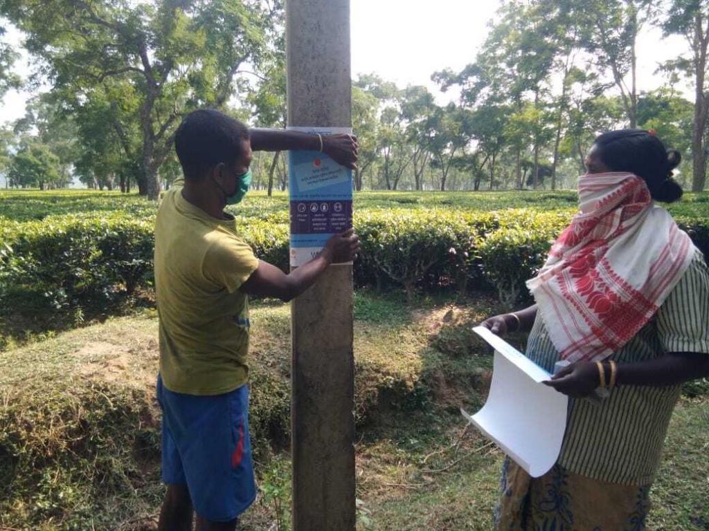 The image shows people putting up campaign posters on a pole.