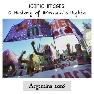 The image shows women protesting and raising slogans while a banner is above them. 